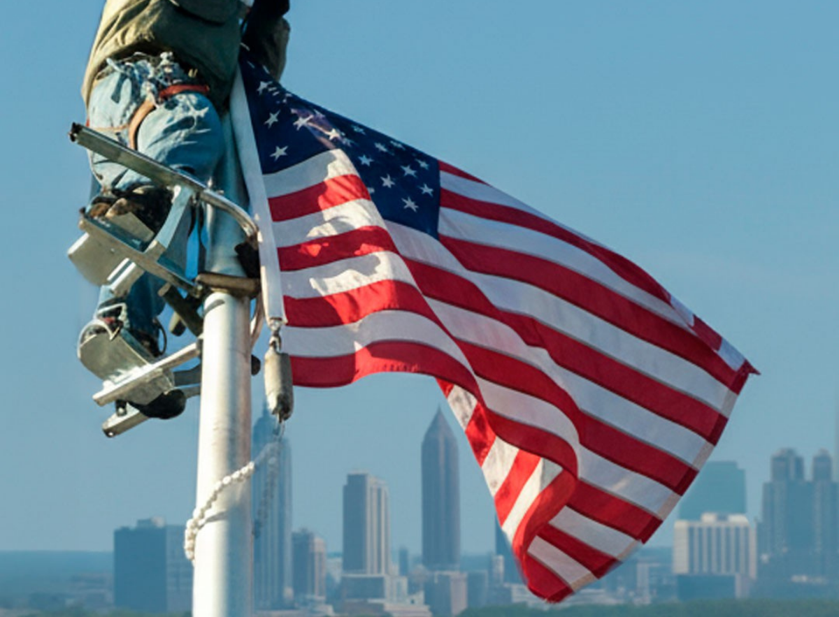 Flagpole climber with American flag and city skyline in the background